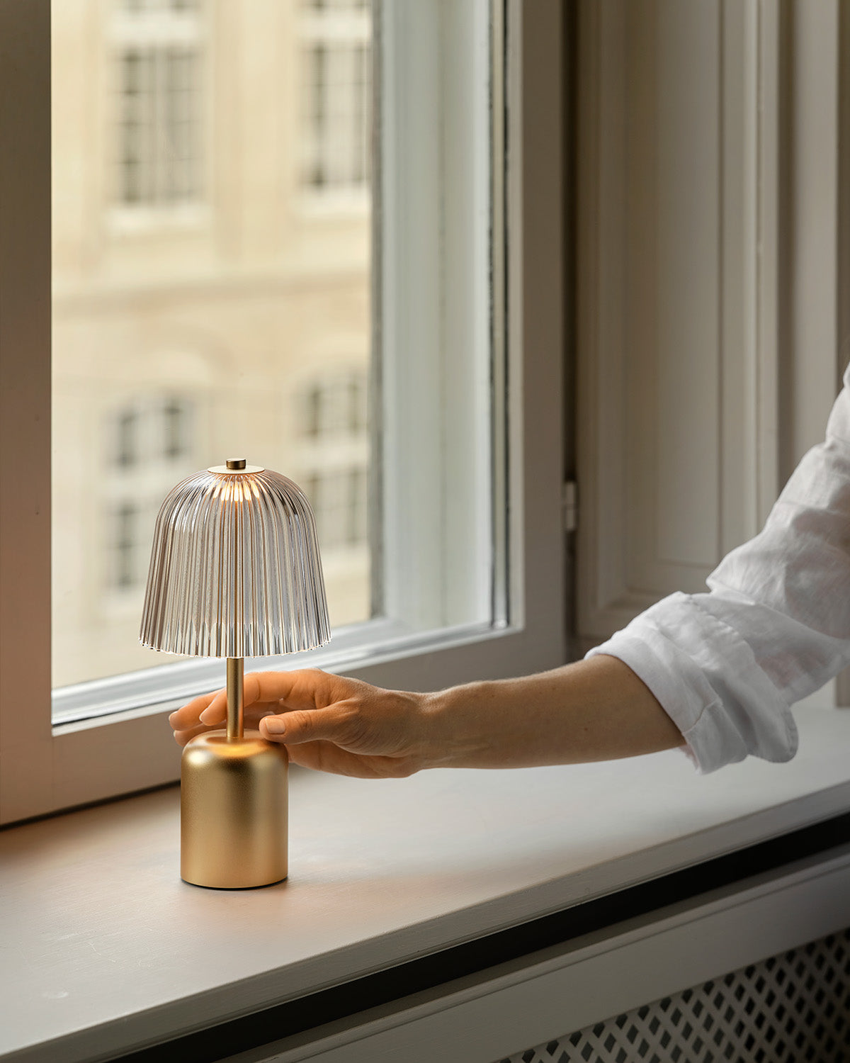 Person holding a small, portable table lamp in gold near a window.