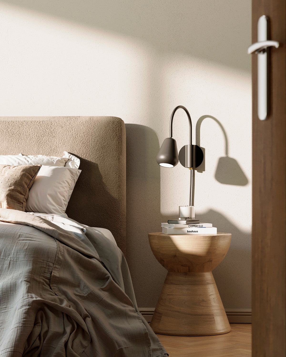 Anoli Spot Wall in black in a bedroom scene with a bed, lamp on a wooden side table, and neutral wall. Minimalistic and Scandinavian.