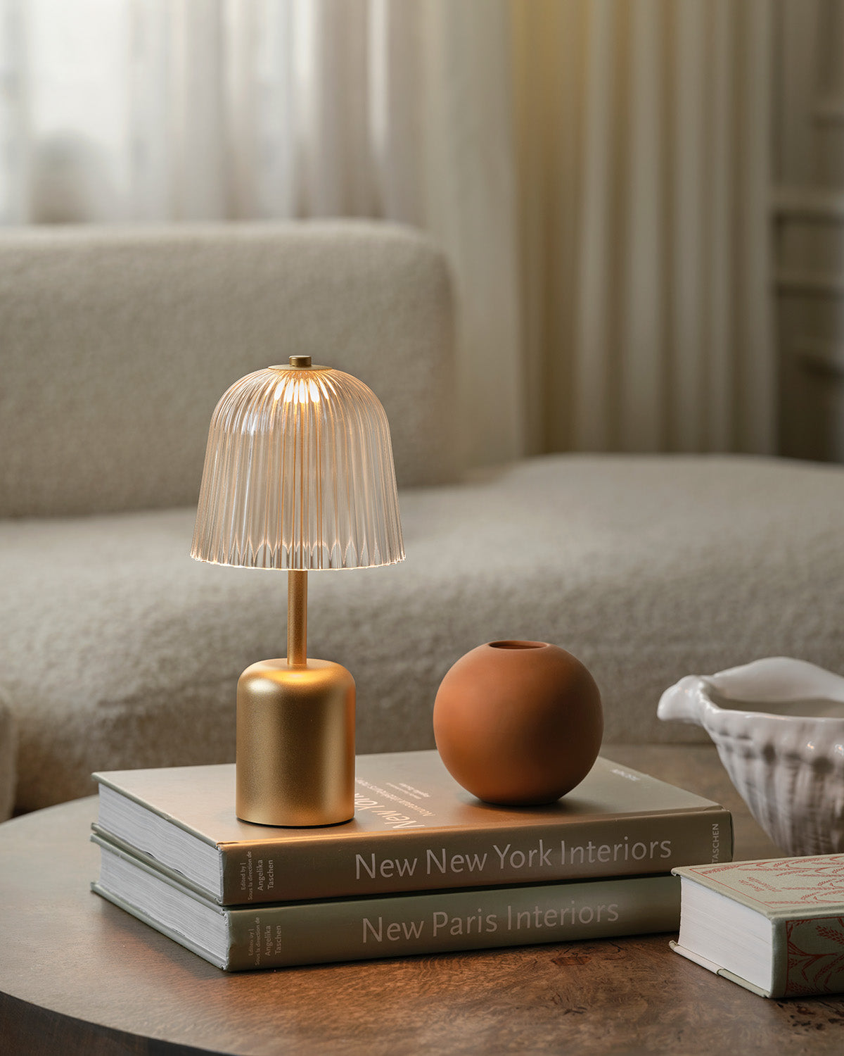 Small gold lamp with crystal clear lamp shade on coffee table books in a living room